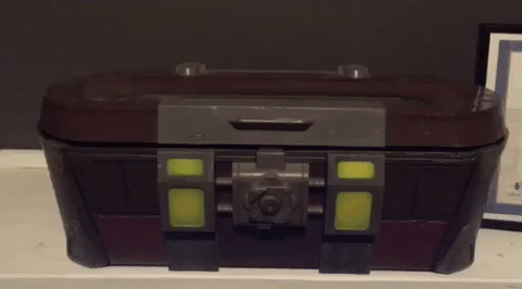 Short animated clip of a cat hiding inside a toy treasure box. A hand reaches for the box, prompting the cat to open the lid and slap the hand.