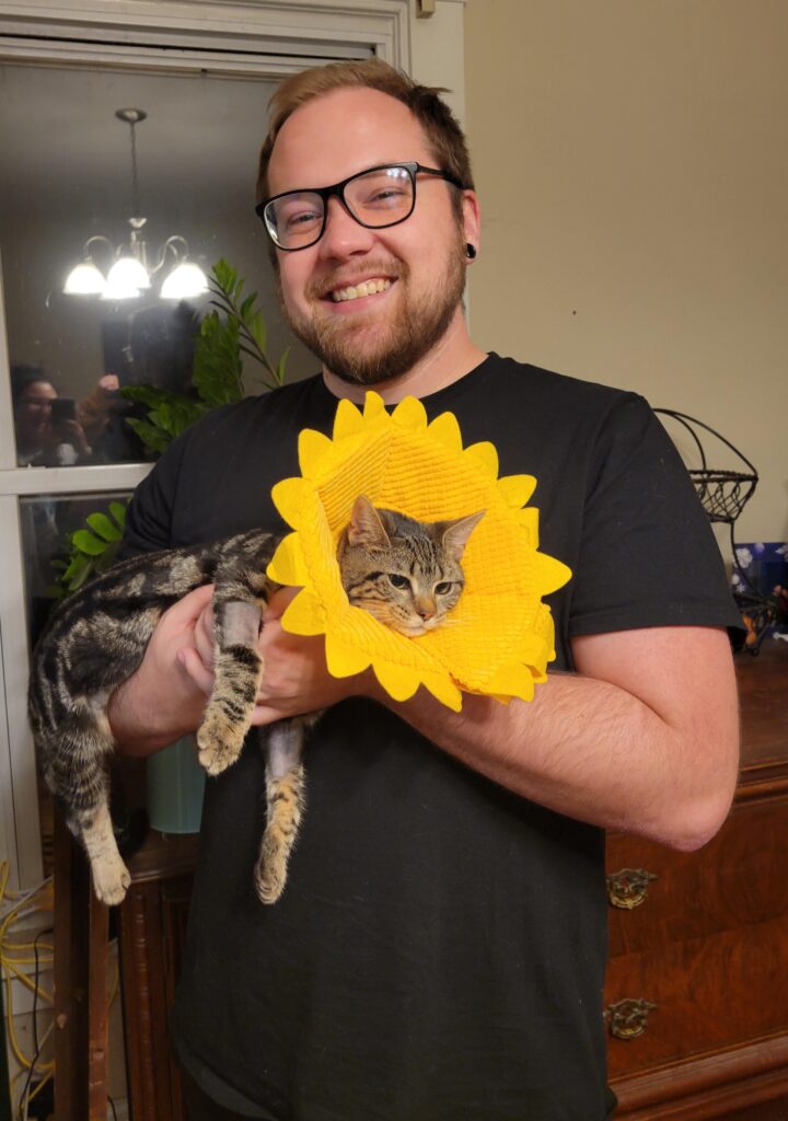 Man holds cat wearing sunflower shaped cone of shame