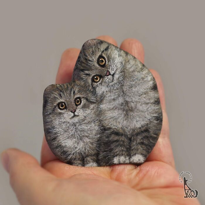 Hand holds a rock onto which two realistic looking kittens have been painted