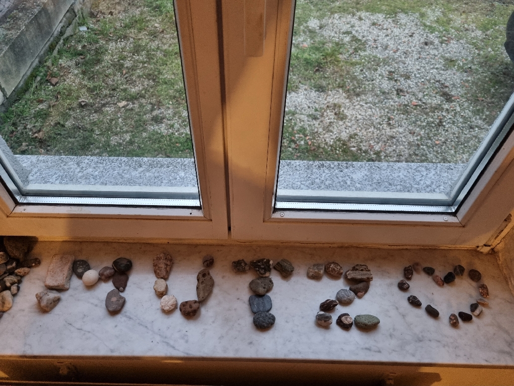 On a windowsill, small rocks are grouped to spell "mutz" and a valentine heart.