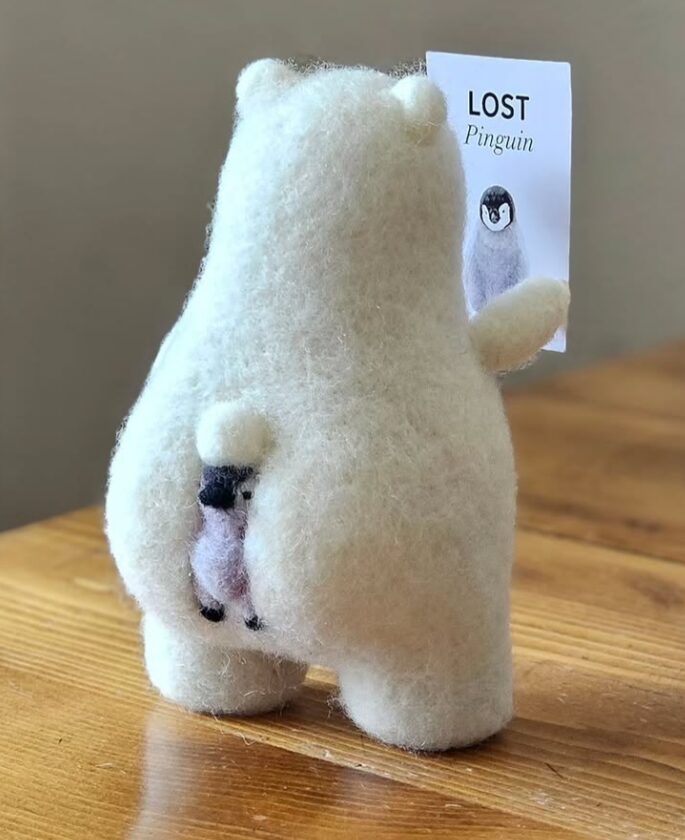 Handcrafted felt art depicting a polar bear reading a sign that says "lost penguin." The penguin shown on the poster is wedged in the bear's butt cheeks.